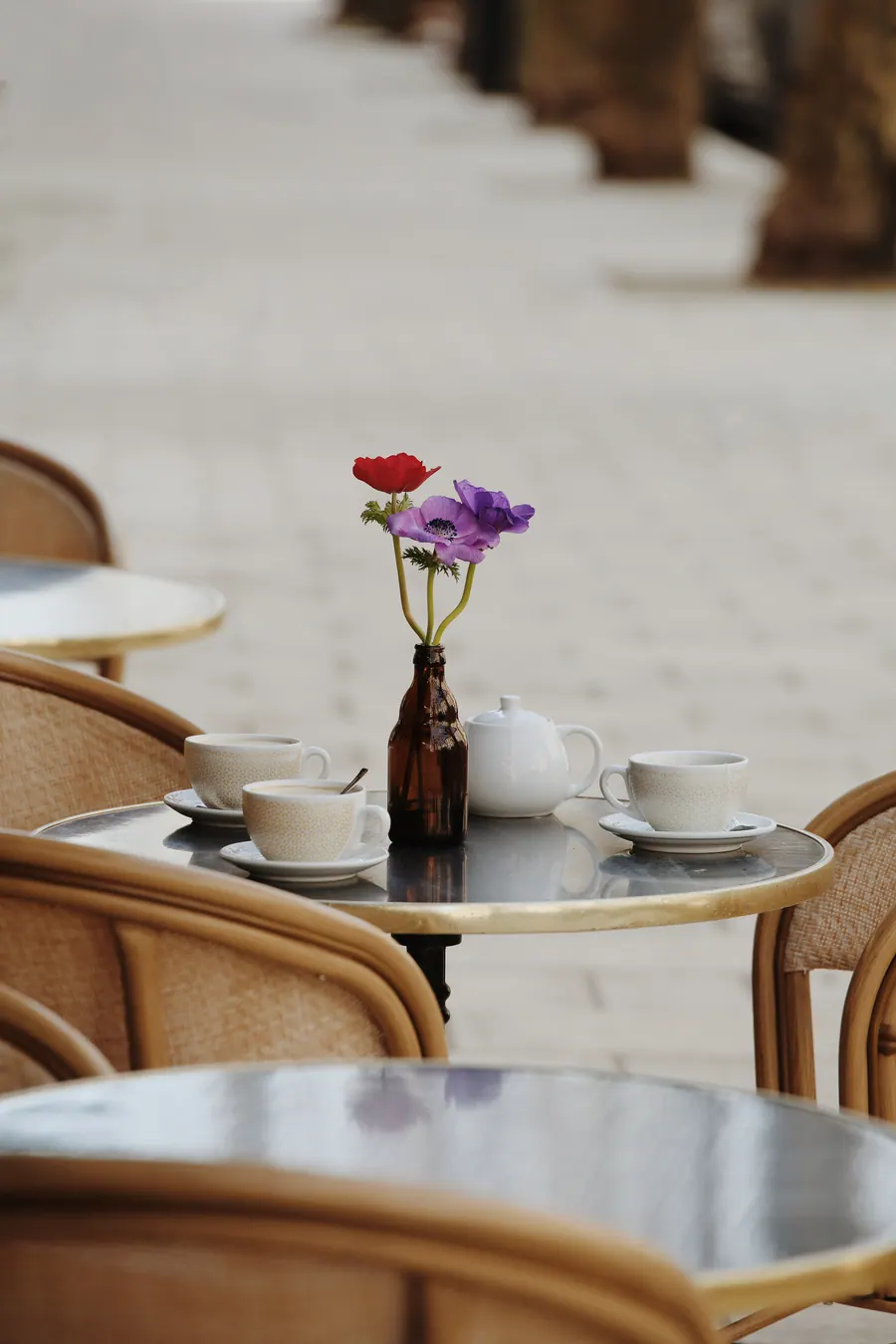 Cafés et théière sur un guéridon de terrasse, bouquet d'anémones